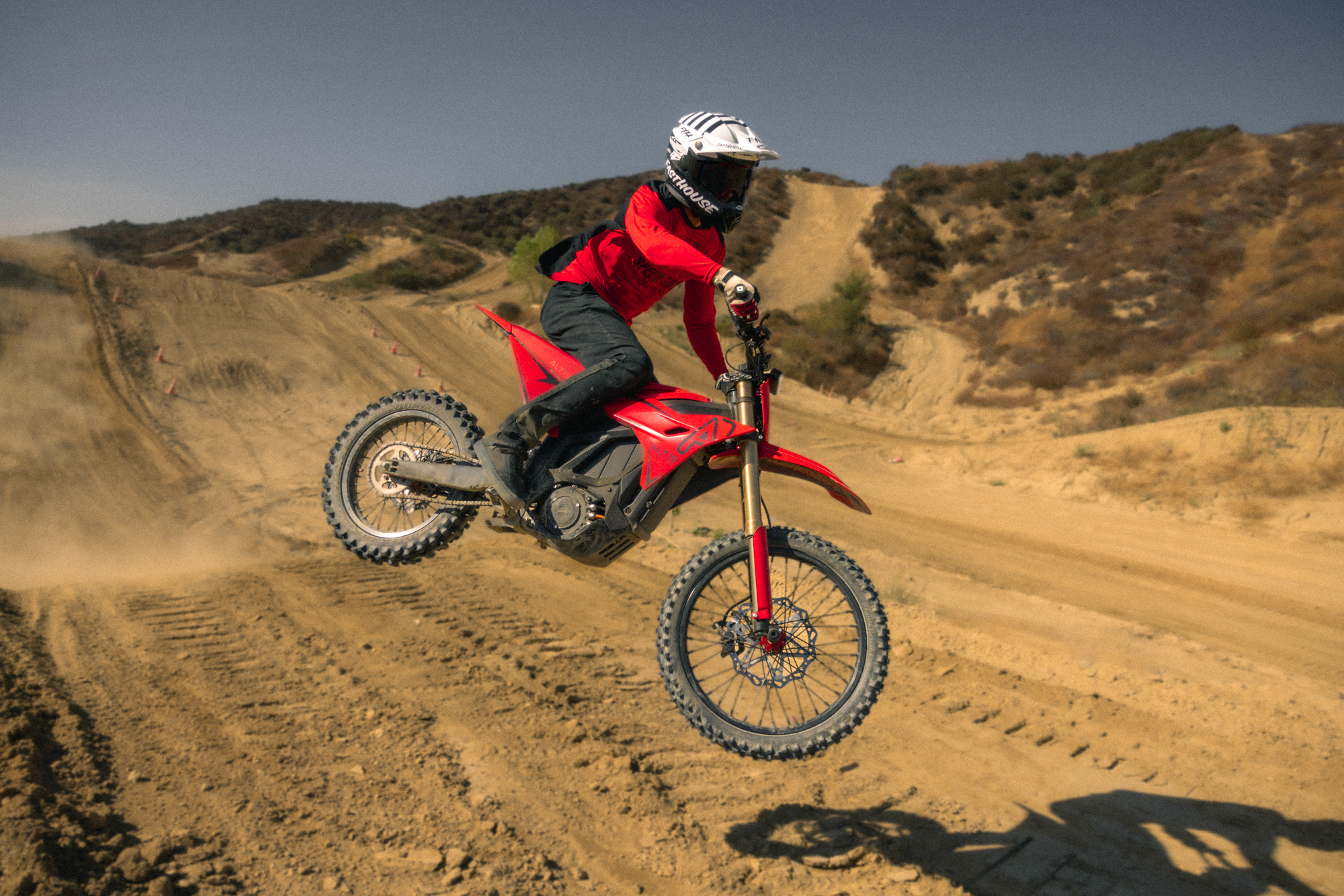 Motocross rider in red gear jumping the Altis Sigma electric dirt bike on desert terrain